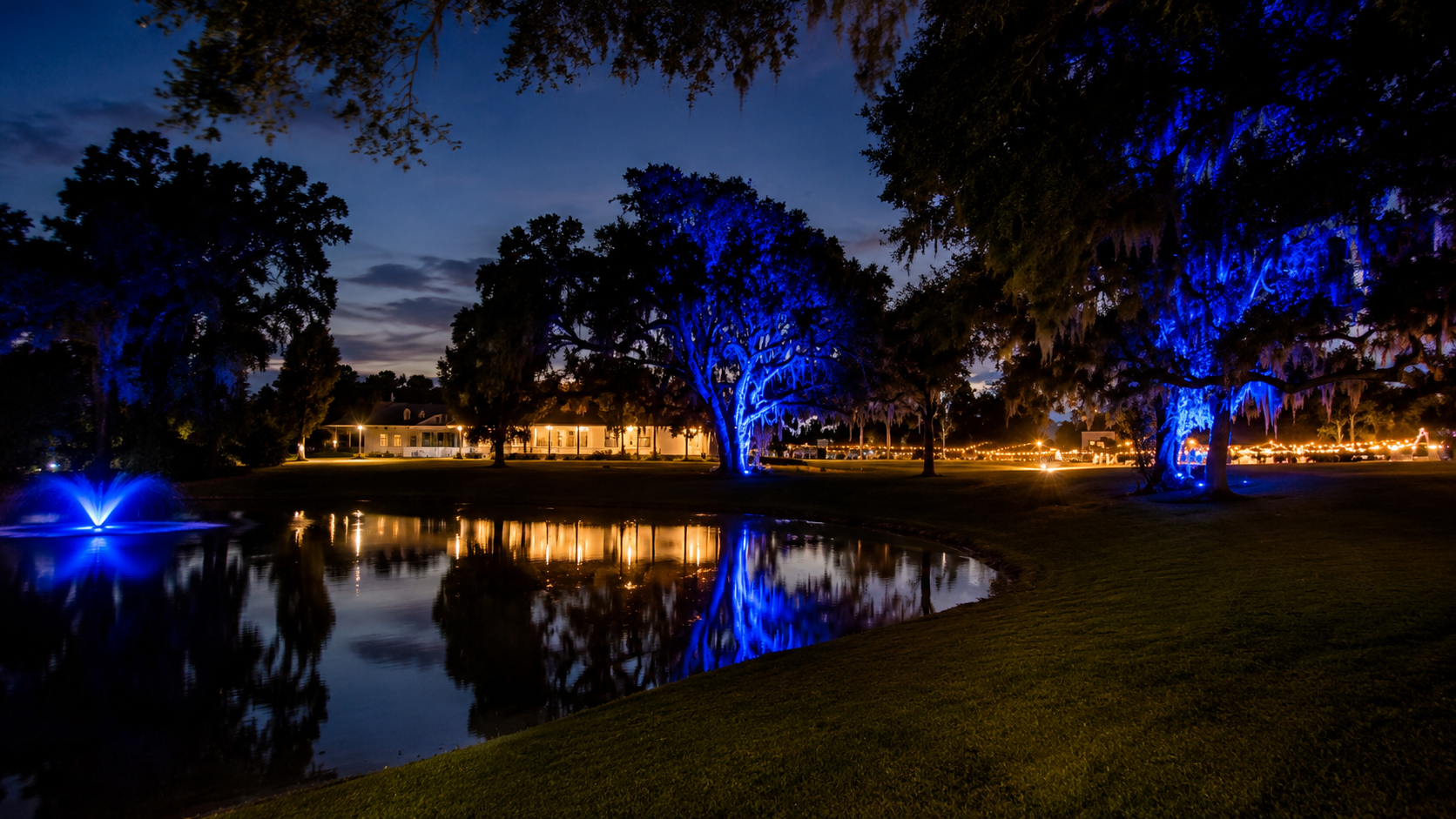 The Ranch estate at night with blue-lit oak trees and pond reflection