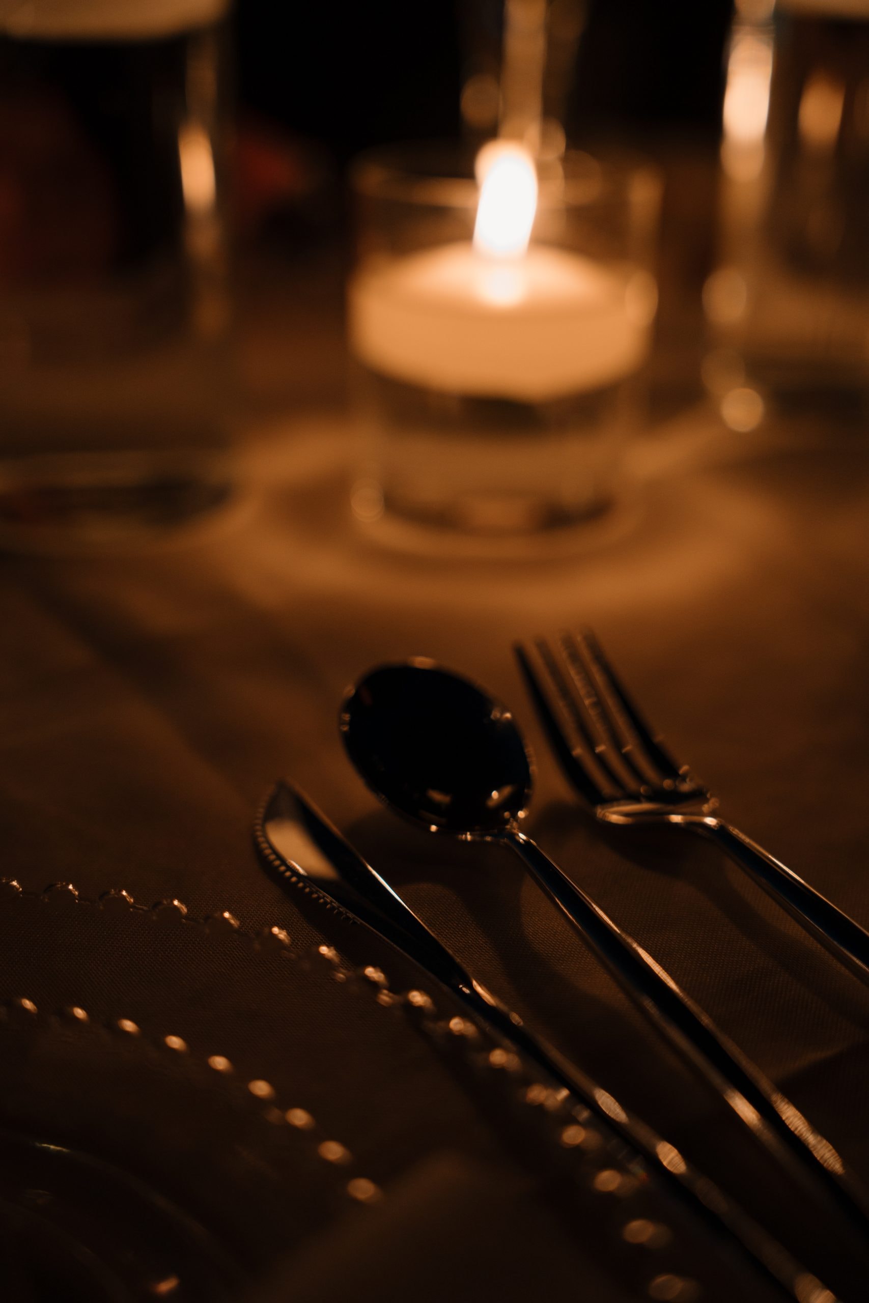 Close-up of an elegant candlelit place setting with silverware and glowing candles on a dark linen table