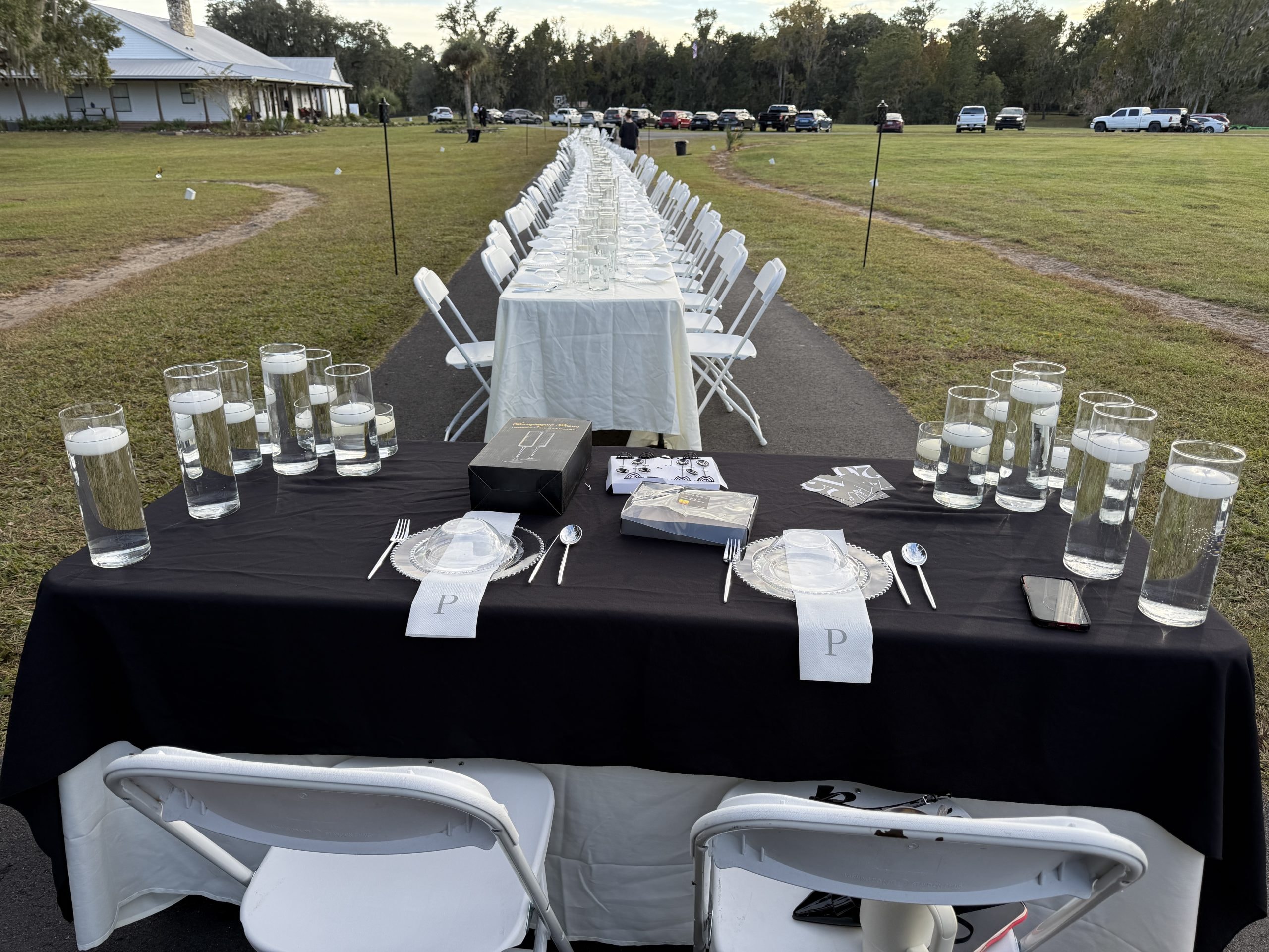 Long outdoor banquet table with black linens, floating candles, and white chairs stretching across the ranch grounds