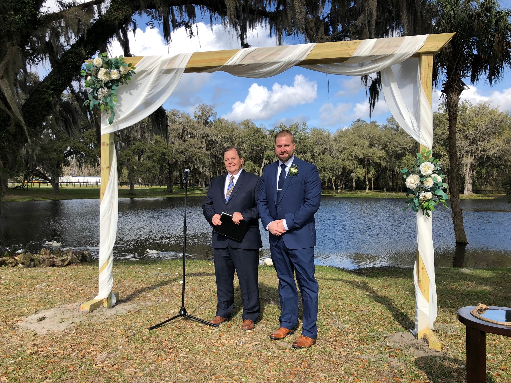 Outdoor wedding ceremony under a draped arbor by the lake with Spanish moss trees