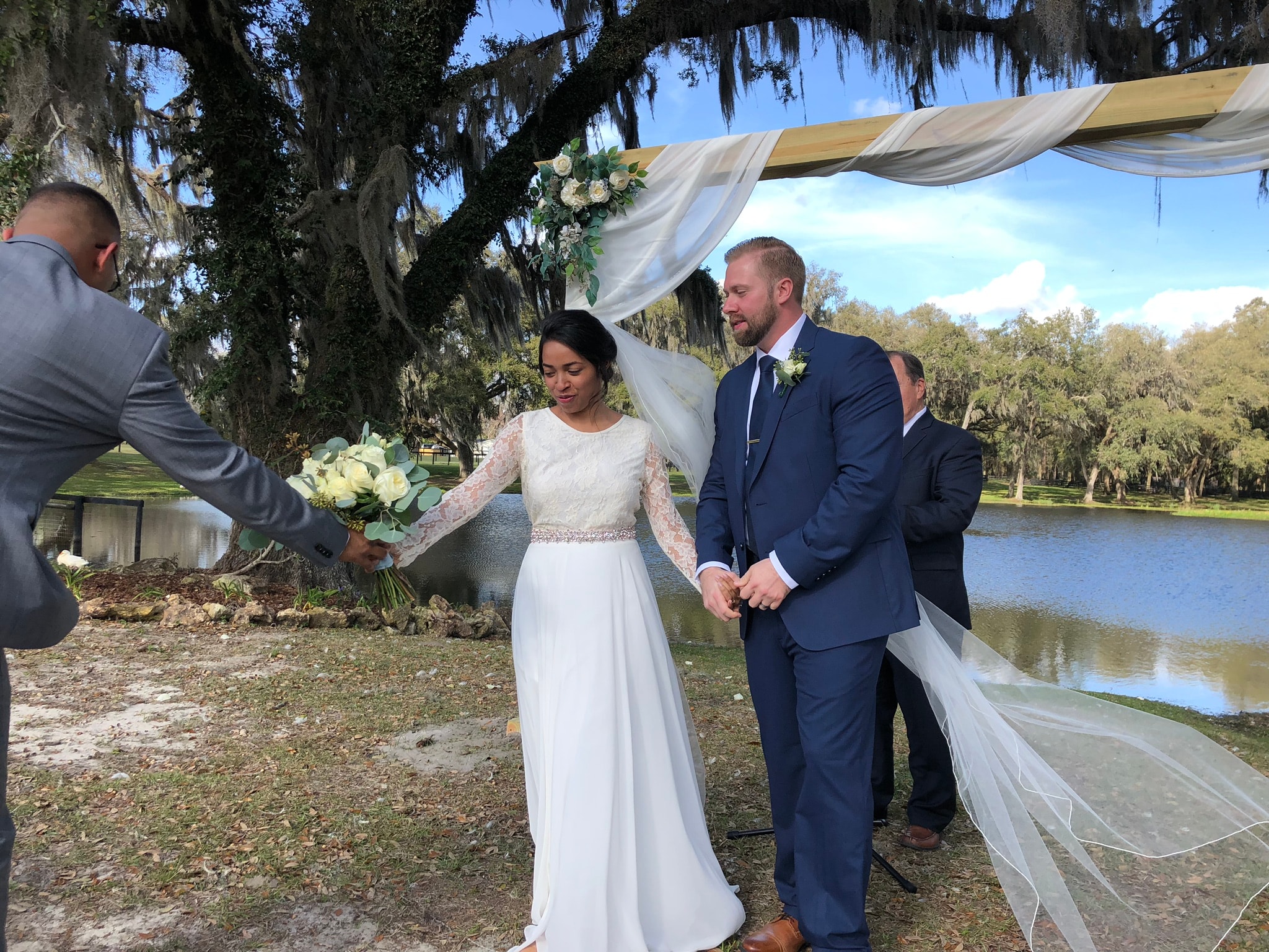 Bride and groom exchanging vows at lakeside arbor with Spanish moss canopy
