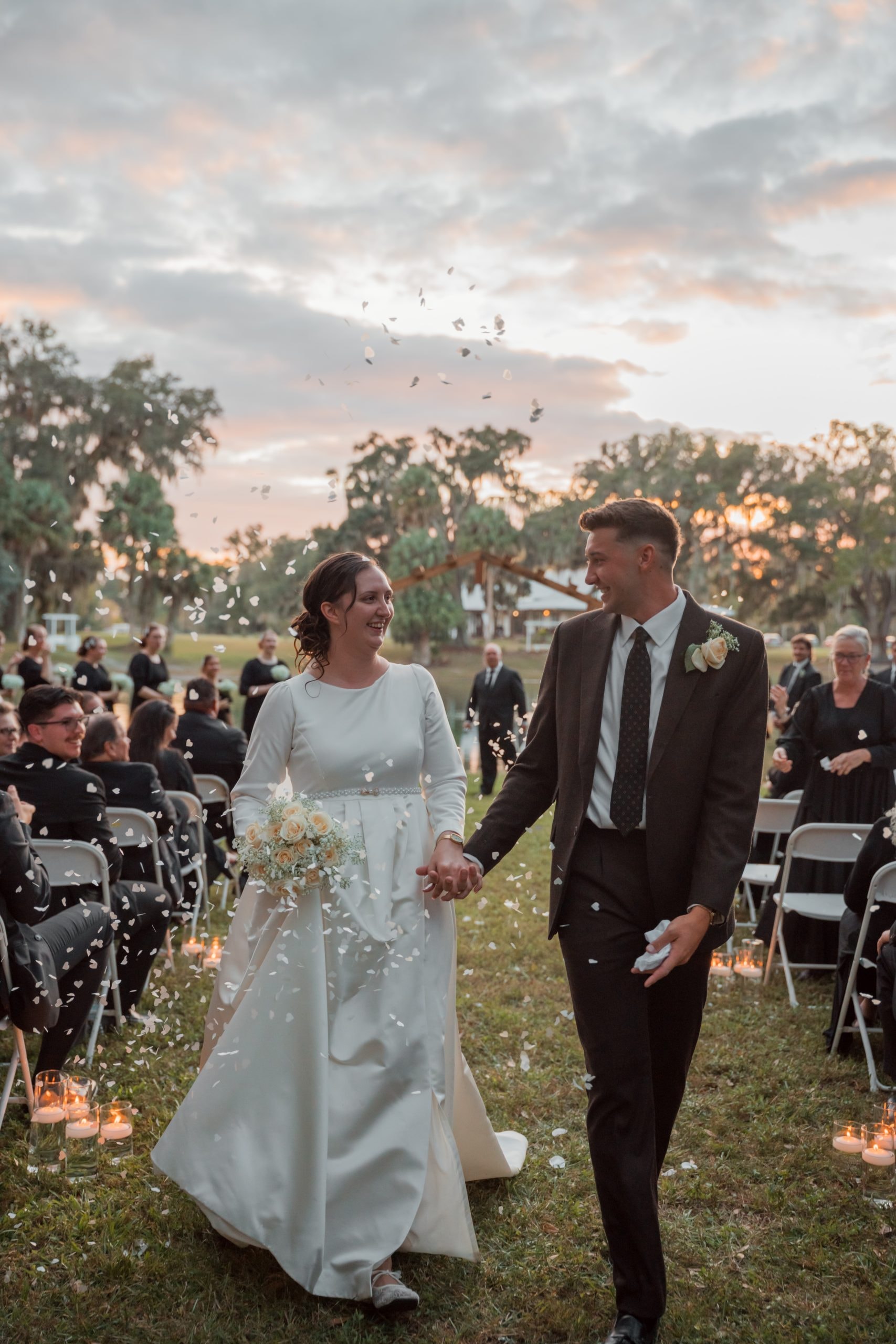 Newlyweds walking the recessional aisle with confetti and candlelit path at sunset