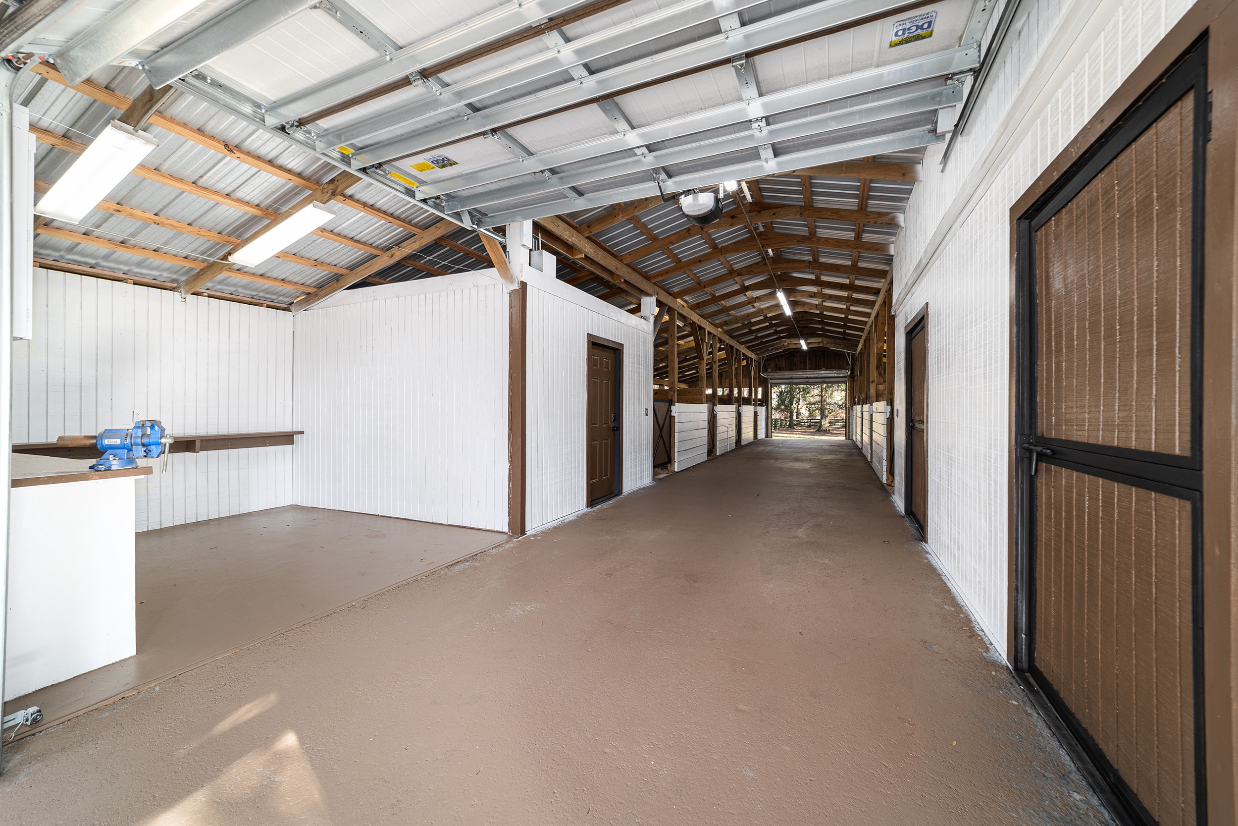 Wide interior view of the ranch barn showing the open aisle, stall doors, and vaulted metal roof with skylights