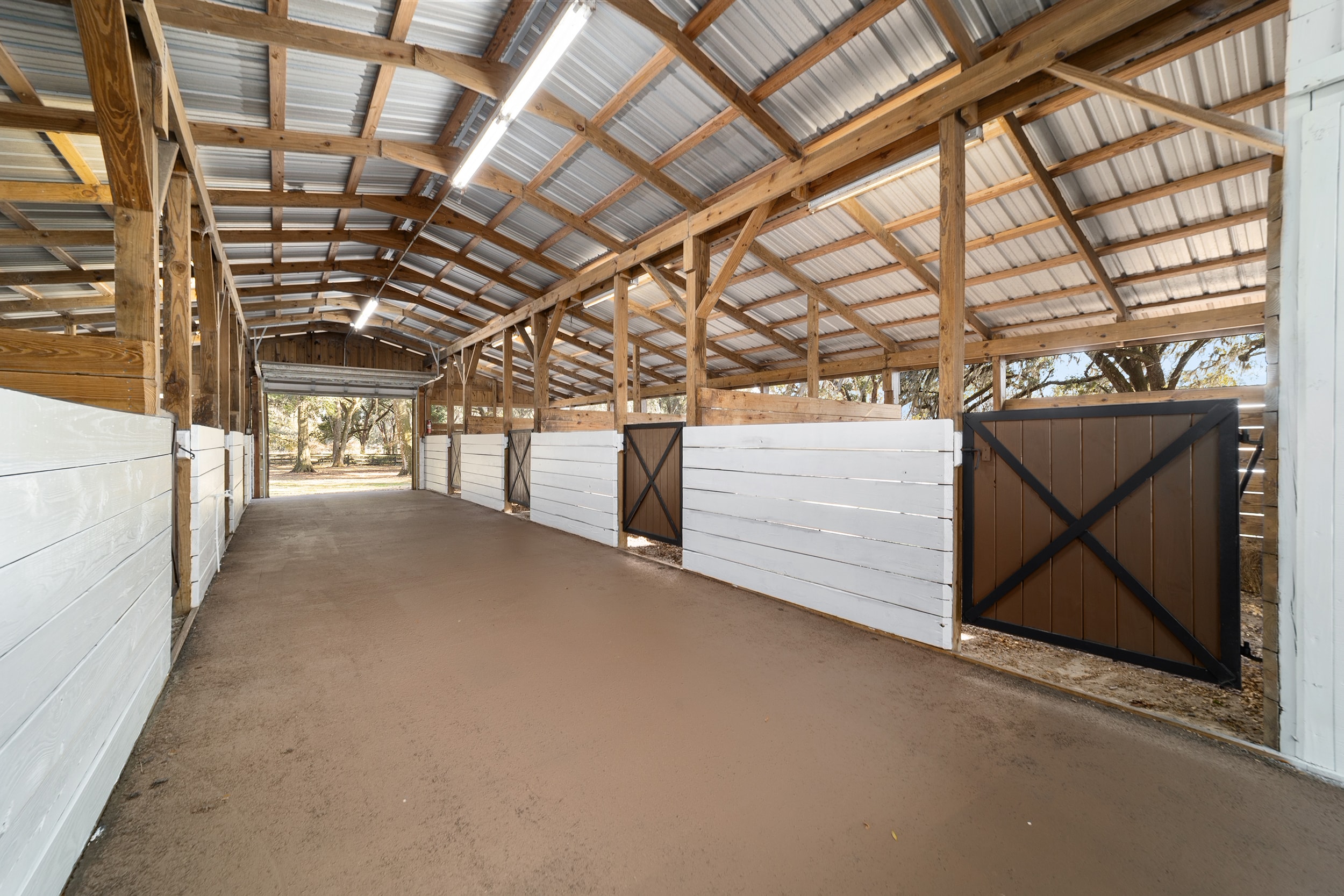 Interior of the ranch barn with white-painted stalls, dark cross-brace doors, and open timber roof structure