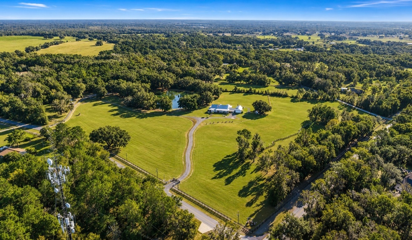 Close aerial view of the white farmhouse estate with metal roof, manicured grounds, and circular driveway