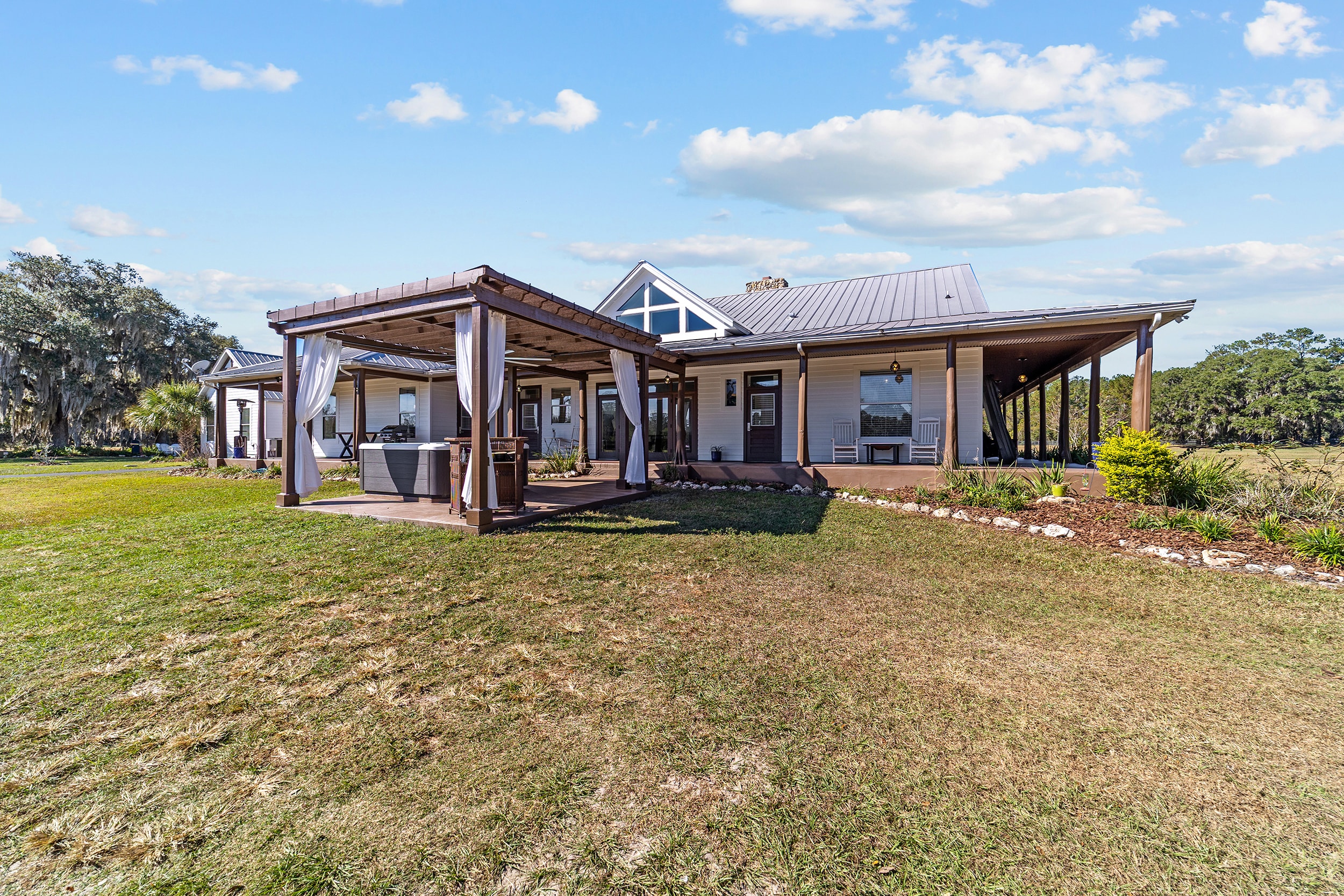 Back view of the ranch estate with pergola, hot tub, wraparound porch, and open pasture stretching to the horizon