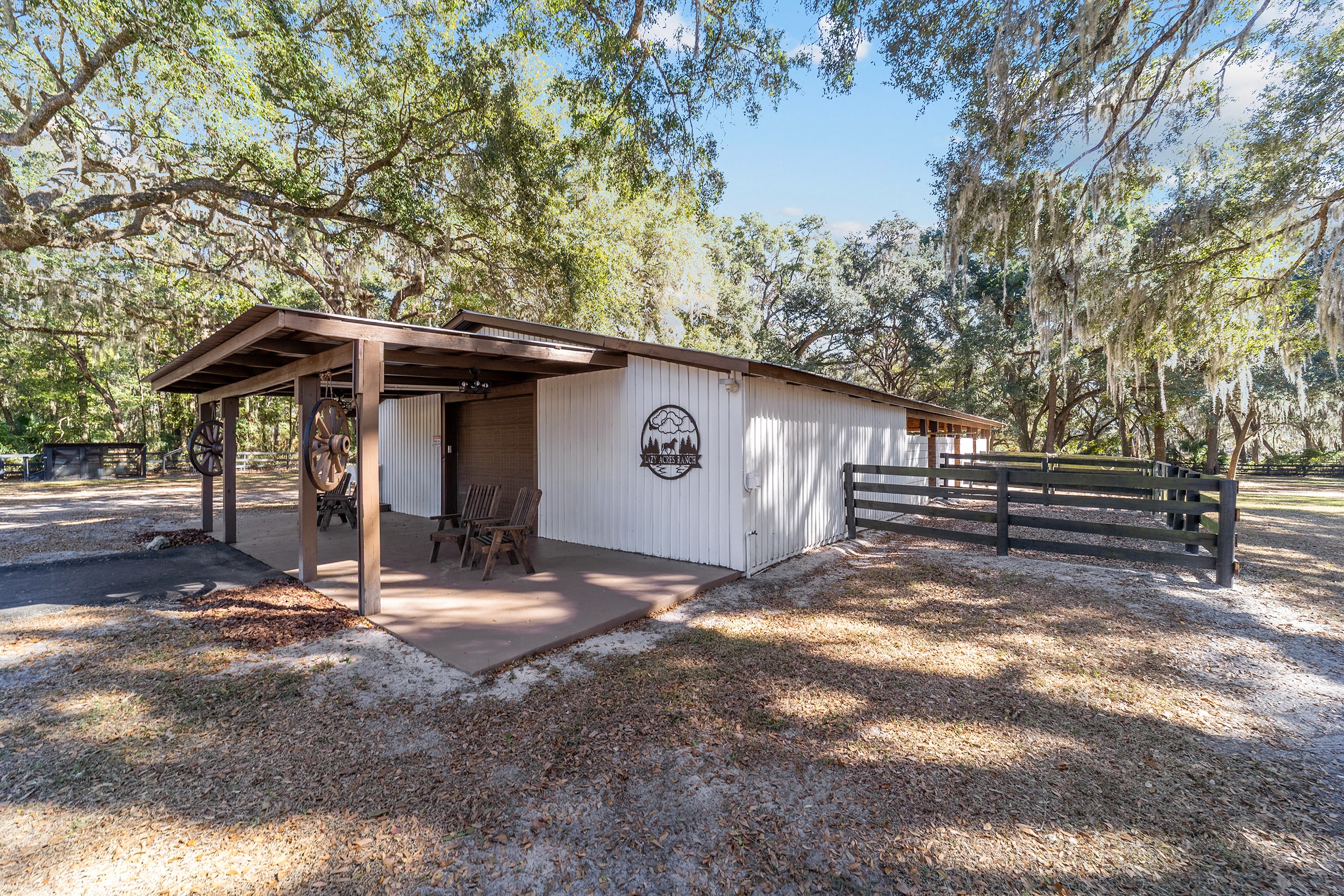 Ranch outbuilding with covered porch, wagon wheel decor, and the Lazy Acres Ranch logo sign under Spanish moss oaks